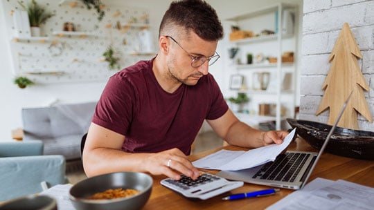 Man looks at paperwork and uses calculator.
